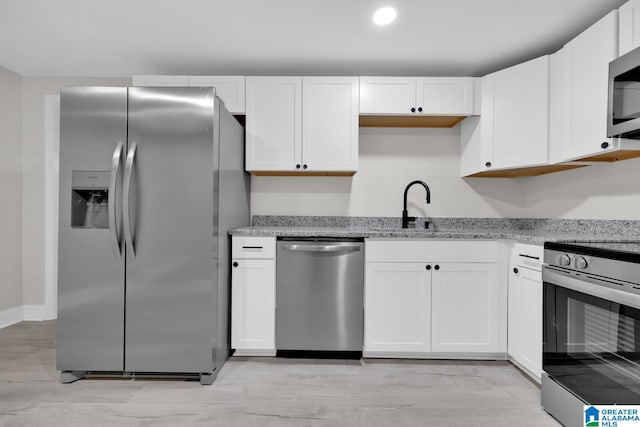 kitchen featuring light stone countertops, white cabinets, sink, light hardwood / wood-style flooring, and appliances with stainless steel finishes