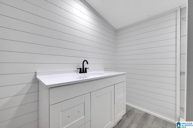 bathroom featuring lofted ceiling, wood-type flooring, wood walls, and vanity