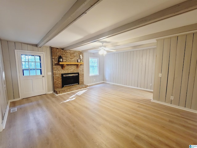 unfurnished living room featuring light wood-type flooring, a fireplace, beamed ceiling, and a wealth of natural light