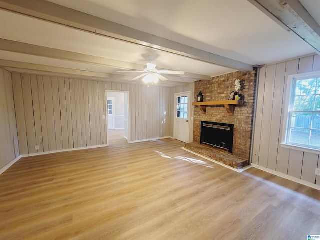 unfurnished living room with light wood-style floors, beamed ceiling, a fireplace, a ceiling fan, and baseboards
