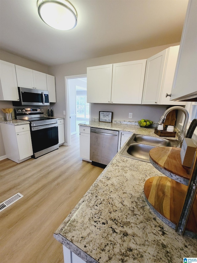kitchen featuring visible vents, a sink, appliances with stainless steel finishes, white cabinetry, and light wood finished floors