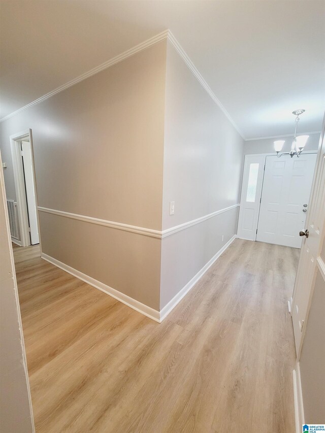 corridor with crown molding, light wood-style flooring, and a notable chandelier