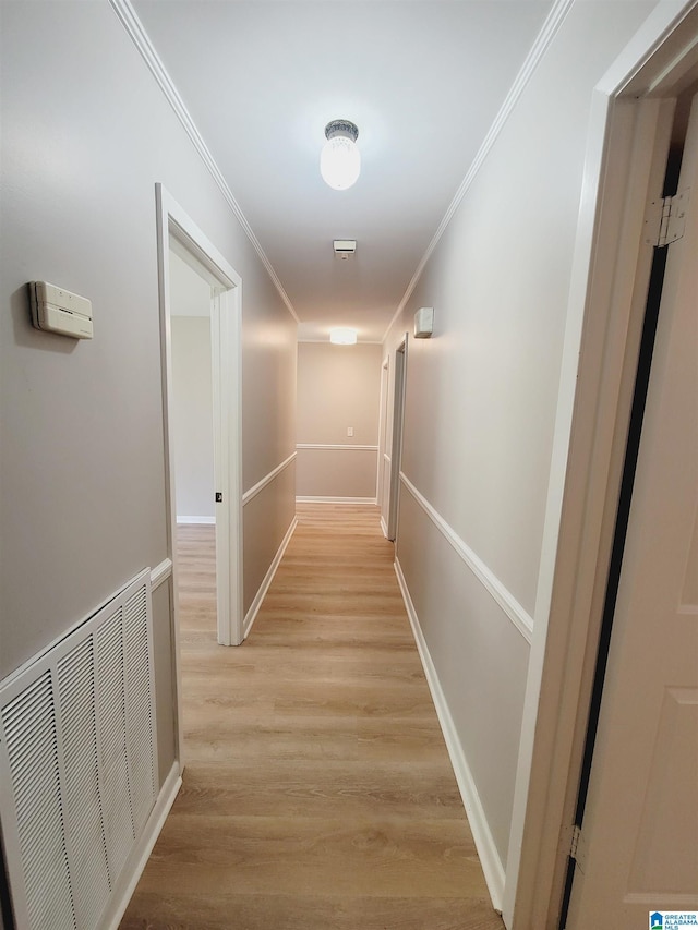corridor featuring light wood-style floors, visible vents, baseboards, and ornamental molding