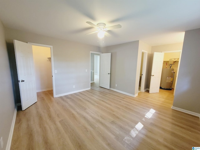 unfurnished bedroom featuring water heater, baseboards, a spacious closet, ceiling fan, and light wood finished floors