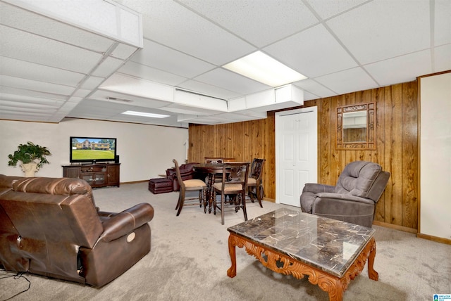 carpeted living room featuring a drop ceiling and wood walls