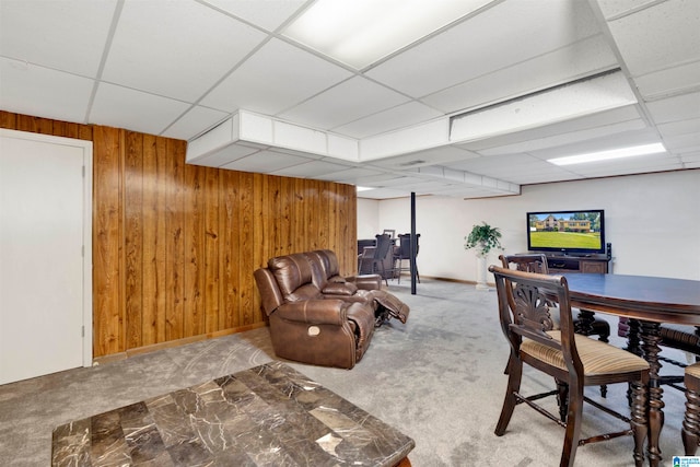 carpeted living room featuring a drop ceiling and wooden walls