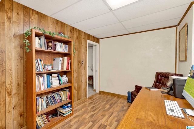 office featuring light wood-type flooring, a paneled ceiling, and wooden walls