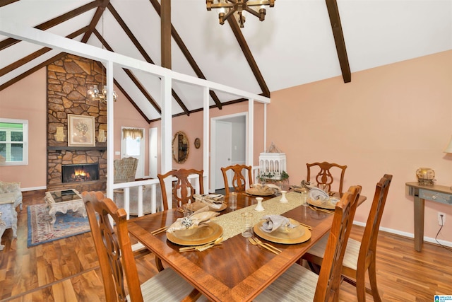 dining room featuring high vaulted ceiling, wood-type flooring, beamed ceiling, and a stone fireplace