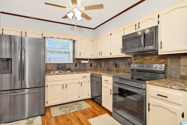 kitchen featuring appliances with stainless steel finishes, decorative backsplash, cream cabinetry, light hardwood / wood-style flooring, and sink