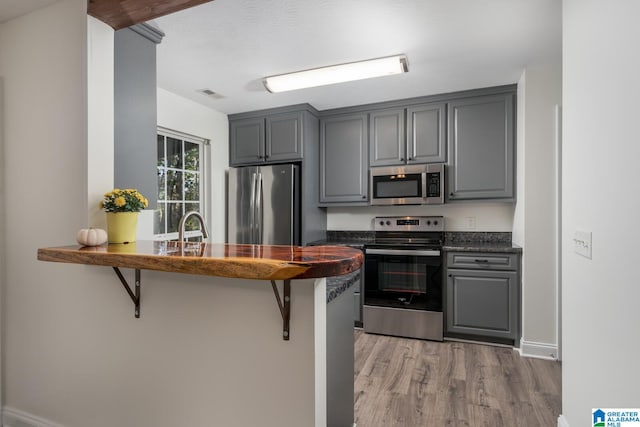 kitchen with gray cabinetry, a kitchen bar, stainless steel appliances, and light hardwood / wood-style flooring