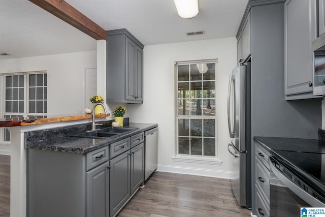 kitchen with gray cabinetry, sink, stainless steel appliances, kitchen peninsula, and hardwood / wood-style flooring