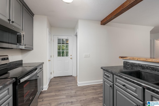 kitchen with beamed ceiling, gray cabinetry, a textured ceiling, stainless steel appliances, and light wood-type flooring