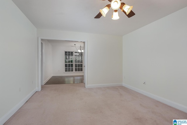 carpeted spare room featuring ceiling fan with notable chandelier