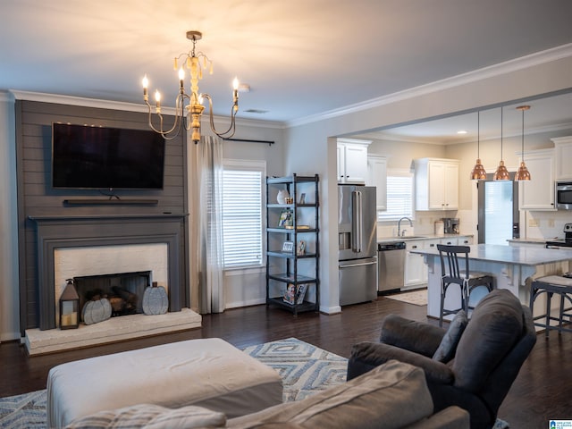 living room with ornamental molding, sink, a brick fireplace, a notable chandelier, and dark hardwood / wood-style flooring