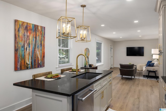 kitchen with an island with sink, sink, decorative light fixtures, dishwasher, and light wood-type flooring