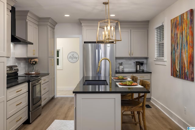 kitchen featuring wall chimney exhaust hood, sink, light hardwood / wood-style floors, appliances with stainless steel finishes, and a center island with sink