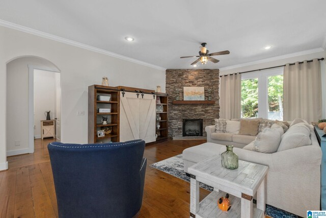 living room featuring ceiling fan, dark hardwood / wood-style flooring, a fireplace, a barn door, and ornamental molding