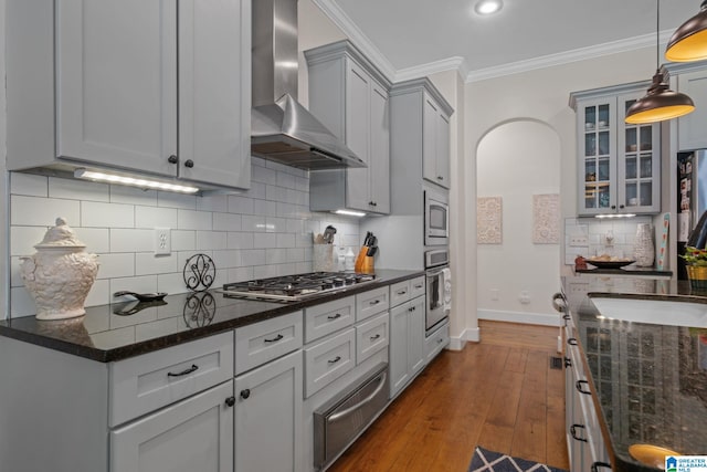 kitchen featuring hanging light fixtures, dark wood-type flooring, wall chimney range hood, stainless steel appliances, and decorative backsplash