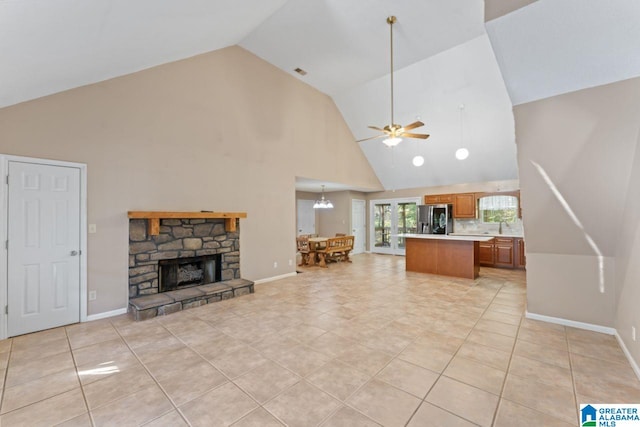 unfurnished living room featuring light tile patterned flooring, ceiling fan with notable chandelier, high vaulted ceiling, and a stone fireplace