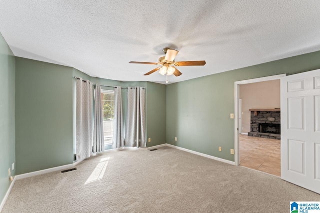 carpeted spare room featuring ceiling fan, a stone fireplace, and a textured ceiling