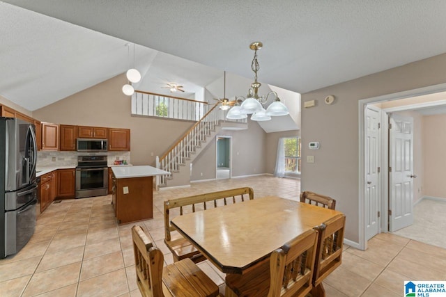 tiled dining space with ceiling fan with notable chandelier, high vaulted ceiling, and a textured ceiling