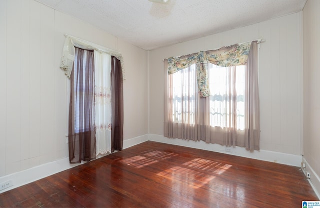 unfurnished room with wooden walls, ceiling fan, dark wood-type flooring, and a textured ceiling