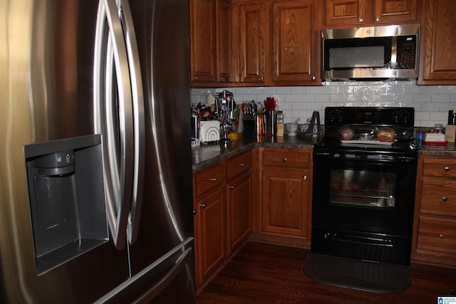 kitchen featuring decorative backsplash, appliances with stainless steel finishes, dark stone countertops, and dark hardwood / wood-style flooring