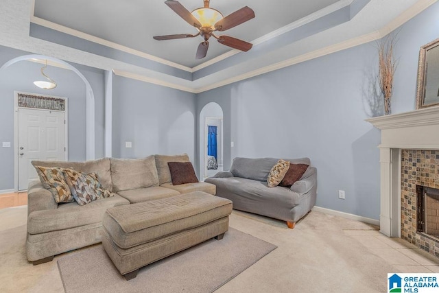 carpeted living room featuring ceiling fan, crown molding, a tray ceiling, and a tile fireplace