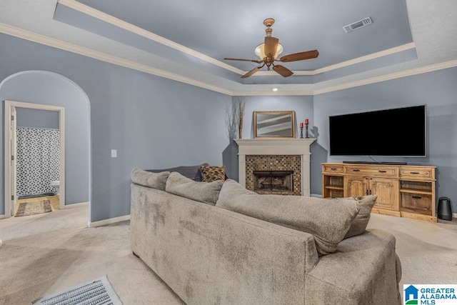 carpeted living room featuring ceiling fan, a tray ceiling, crown molding, and a tile fireplace