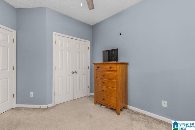 bedroom featuring a closet, light colored carpet, a textured ceiling, and ceiling fan