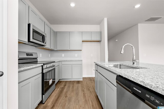 kitchen with sink, light hardwood / wood-style flooring, stainless steel appliances, light stone countertops, and decorative backsplash