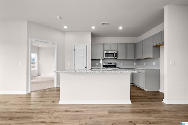 kitchen featuring gray cabinetry, light stone countertops, stainless steel appliances, and a center island with sink