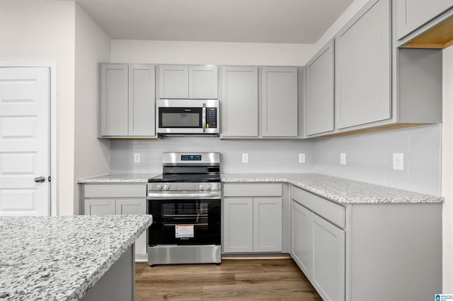 kitchen featuring gray cabinetry, light stone counters, hardwood / wood-style flooring, and appliances with stainless steel finishes