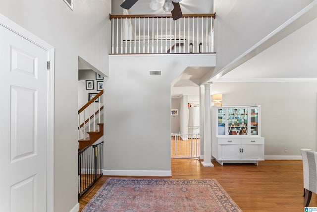 interior space with ceiling fan, hardwood / wood-style flooring, a high ceiling, ornate columns, and crown molding