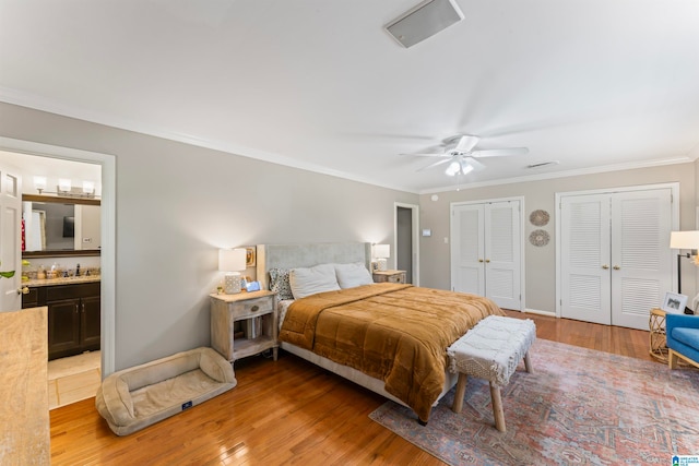 bedroom featuring ceiling fan, two closets, connected bathroom, light hardwood / wood-style flooring, and ornamental molding