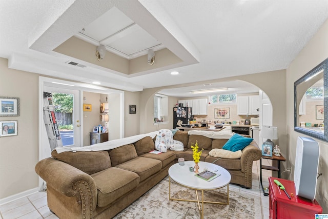 living room with a raised ceiling, plenty of natural light, and light tile patterned floors