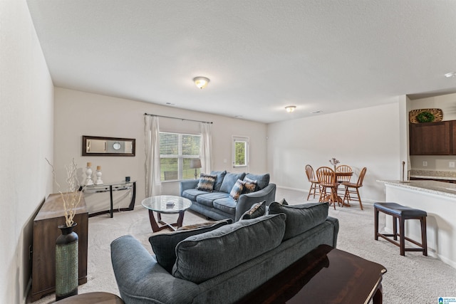 living area featuring light colored carpet, baseboards, and a textured ceiling
