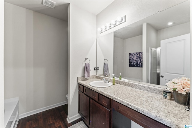 bathroom with wood finished floors, vanity, baseboards, toilet, and a shower with door