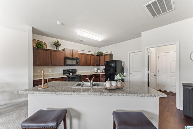 kitchen with black appliances, a sink, a kitchen island with sink, a breakfast bar area, and baseboards