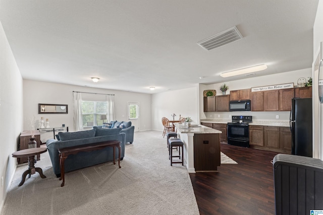kitchen with black appliances, open floor plan, a kitchen bar, a sink, and dark wood-type flooring