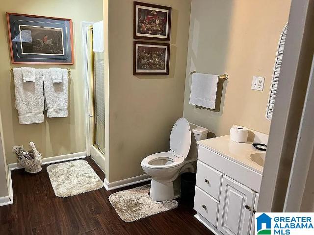 bathroom with hardwood / wood-style floors, toilet, a shower with door, and vanity