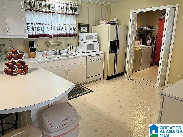 kitchen featuring independent washer and dryer, white appliances, sink, and white cabinetry