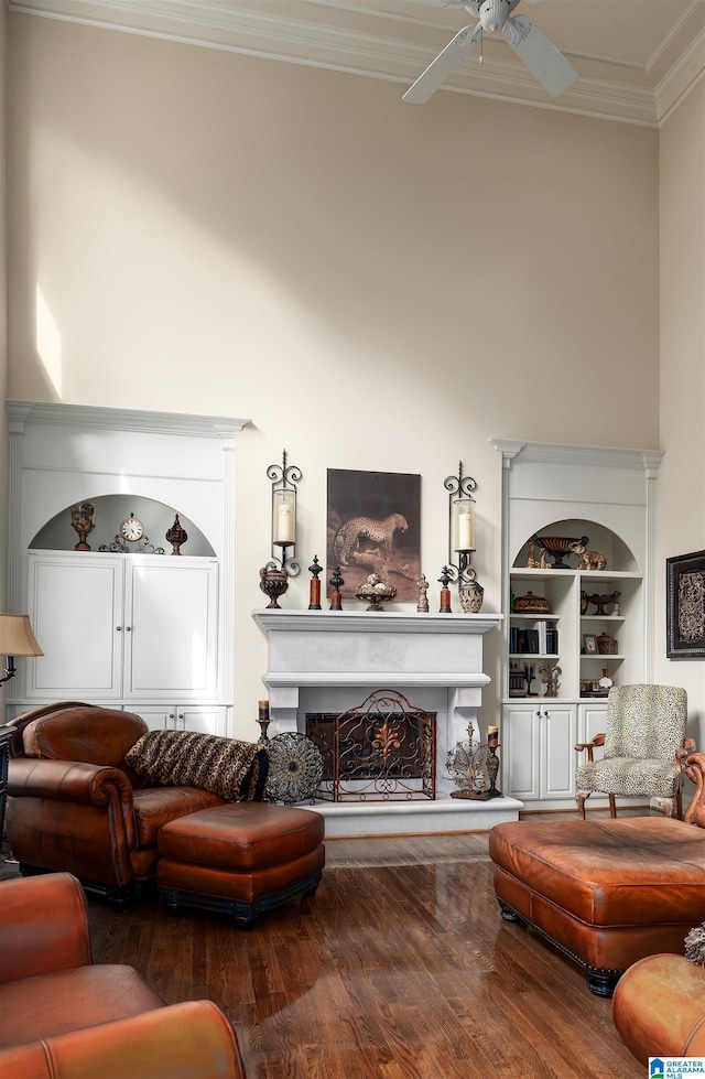 living room featuring crown molding, built in features, wood-type flooring, and ceiling fan