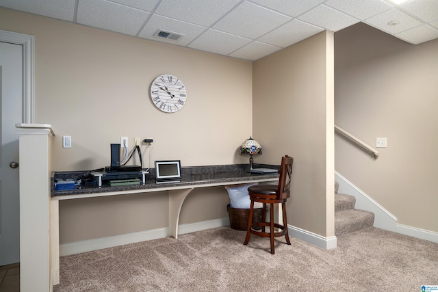 carpeted office space featuring a paneled ceiling and built in desk