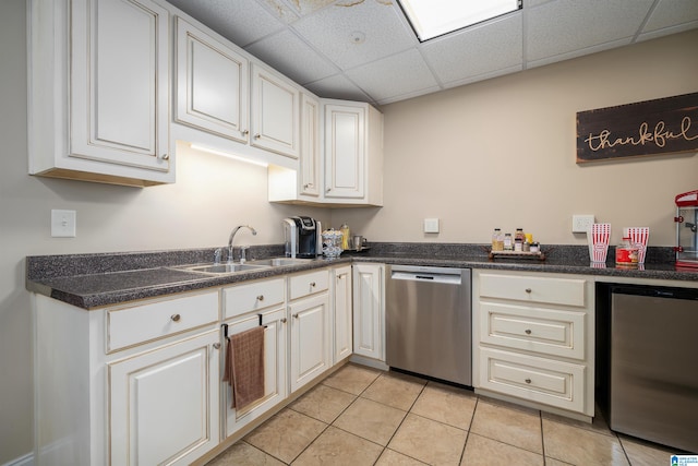 kitchen featuring white cabinets, a paneled ceiling, dishwasher, light tile patterned flooring, and sink