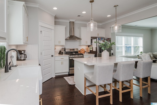 kitchen with hanging light fixtures, wall chimney range hood, white cabinetry, appliances with stainless steel finishes, and dark hardwood / wood-style floors