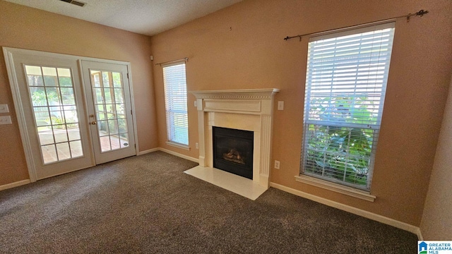 unfurnished living room with french doors, a textured ceiling, plenty of natural light, and dark colored carpet