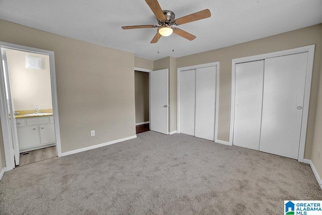 unfurnished bedroom featuring ceiling fan, two closets, sink, ensuite bath, and carpet flooring