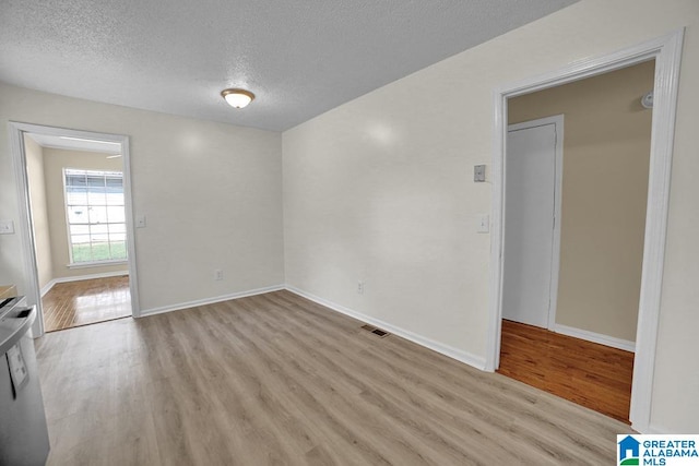 spare room with a textured ceiling and light hardwood / wood-style flooring