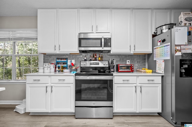 kitchen featuring white cabinets, stainless steel appliances, light wood-type flooring, and decorative backsplash